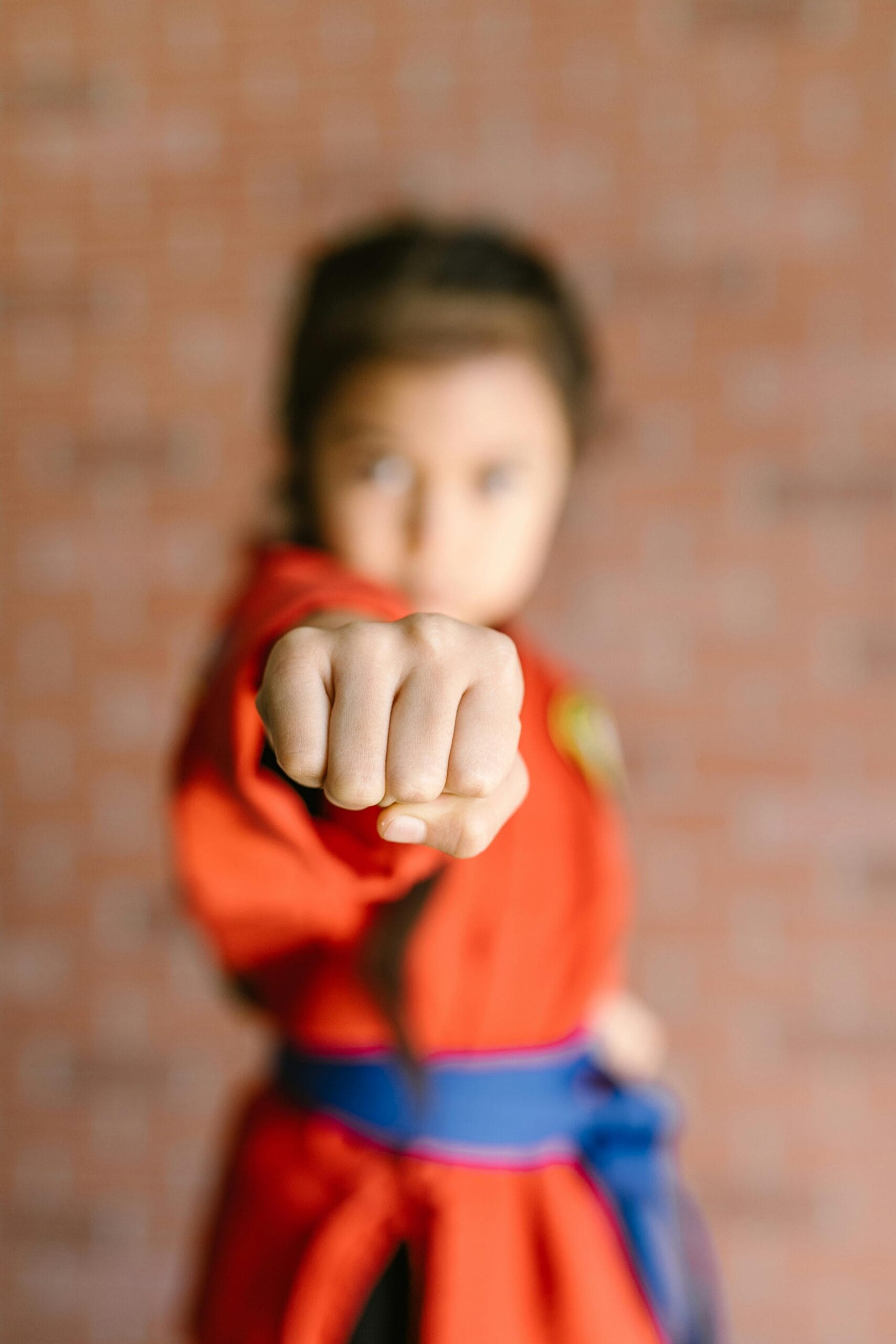 Child in martial arts uniform performs a focused punch indoors.