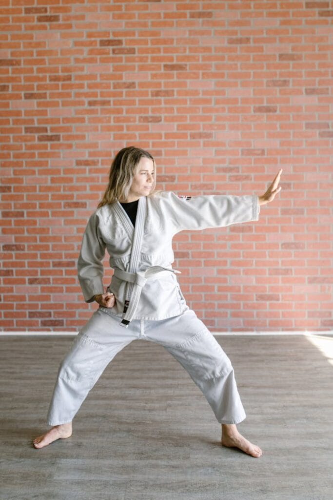 pexels-photo-7045665 Adult woman practicing martial arts in a dojo, wearing a white dobok and belt, posing against a brick wall.