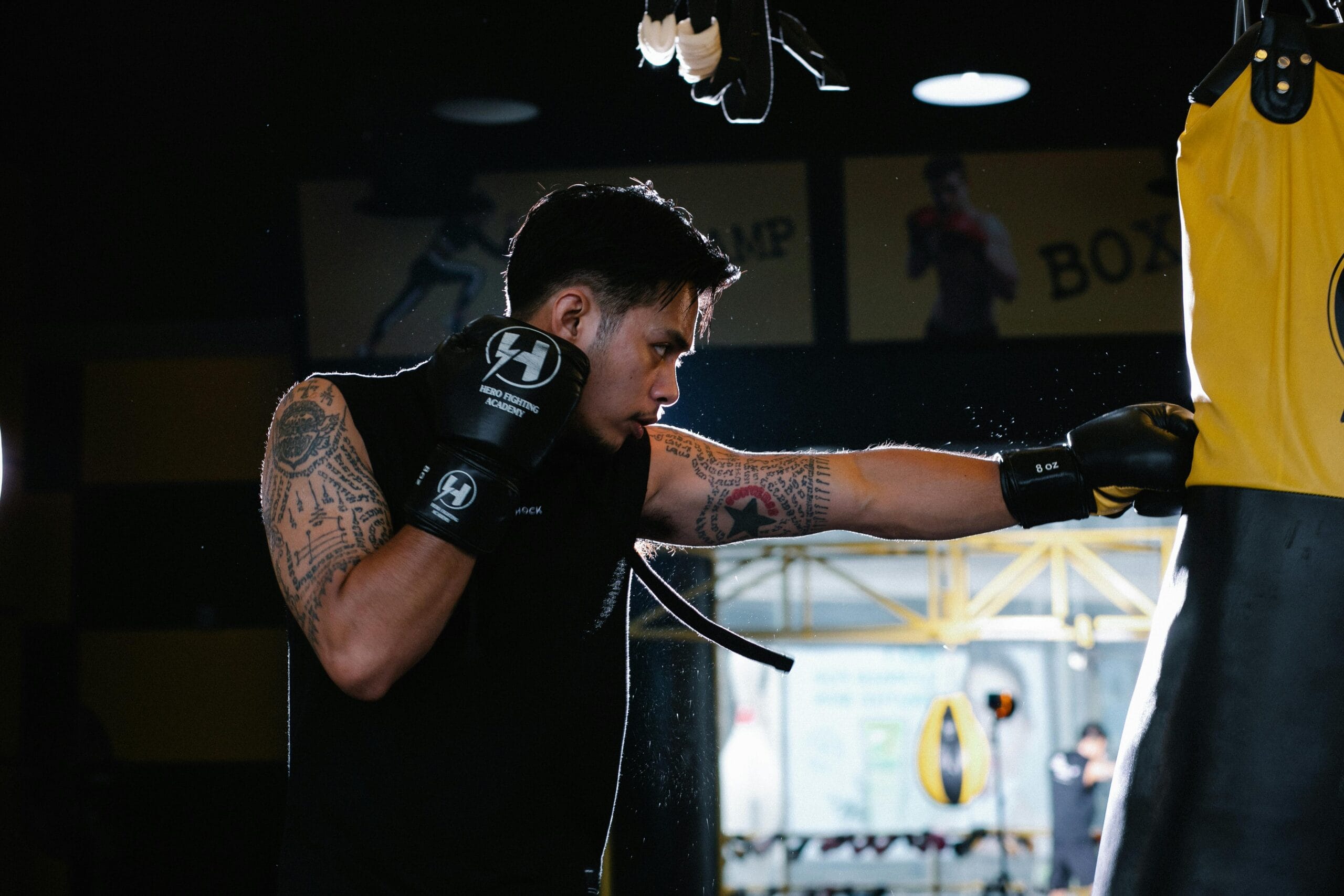 A dedicated boxer with tattoos intensely trains by punching a heavy bag indoors.