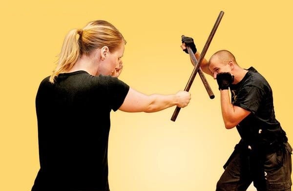 A Kali martial arts practitioner skillfully wielding rattan sticks in a combat stance, showcasing speed, precision, and traditional Filipino techniques.